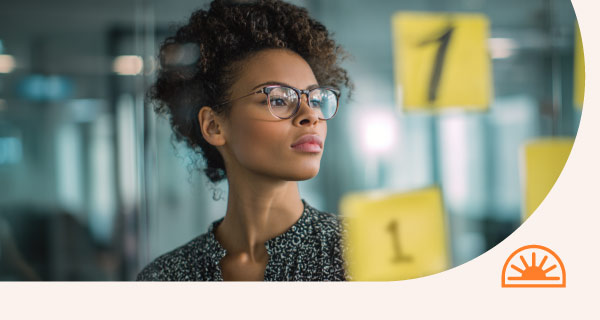 A woman examining a transparent board, containing a sticky note that displays the number 1.
