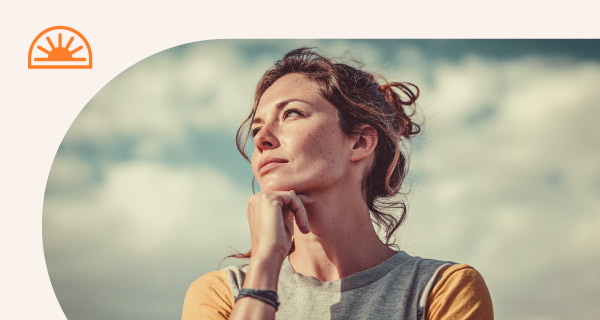 A woman standing outside, resting her chin on her fist.